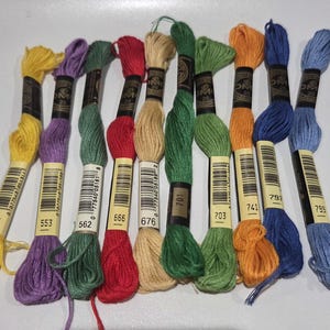 May include: A collection of colorful embroidery floss skeins in various shades of yellow, purple, green, red, tan, orange, blue, and light blue. Each skein has a label with a number. Ideal for embroidery and cross-stitch projects.