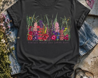 Puede incluir: Una camiseta gris carbón de manga corta con una colorida ilustración estilo acuarela de varias flores silvestres y hierbas. Debajo del diseño floral, el texto "Vielfalt macht das Leben bunt." está impreso en una fuente sencilla y fina.
