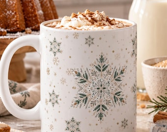 Puede incluir: Una taza de cerámica blanca con un patrón repetitivo de copos de nieve verdes y dorados hechos de ramas de pino. El copo de nieve central incluye las letras F, K, A y F dispuestas en forma de cruz. La taza contiene una bebida caliente cubierta con nata montada y canela.