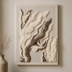 Könnte beinhalten: Texturierte Wandkunst mit einem Design aus abstrakten Formen in Off-White und Braun. Das Kunstwerk hat eine erhabene, taktile Textur auf einem neutralen, leinenfarbenen Hintergrund. Das Stück ist rechteckig und auf einem Holzrahmen montiert.