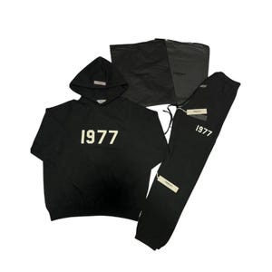Pu&ograve; includere: Set nero composto da felpa con cappuccio e pantaloni della tuta con il numero "1977" stampato in bianco. La felpa ha un cappuccio e una piccola etichetta. I pantaloni della tuta hanno un cordino e un'etichetta. &Egrave; inclusa anche una borsa nera.