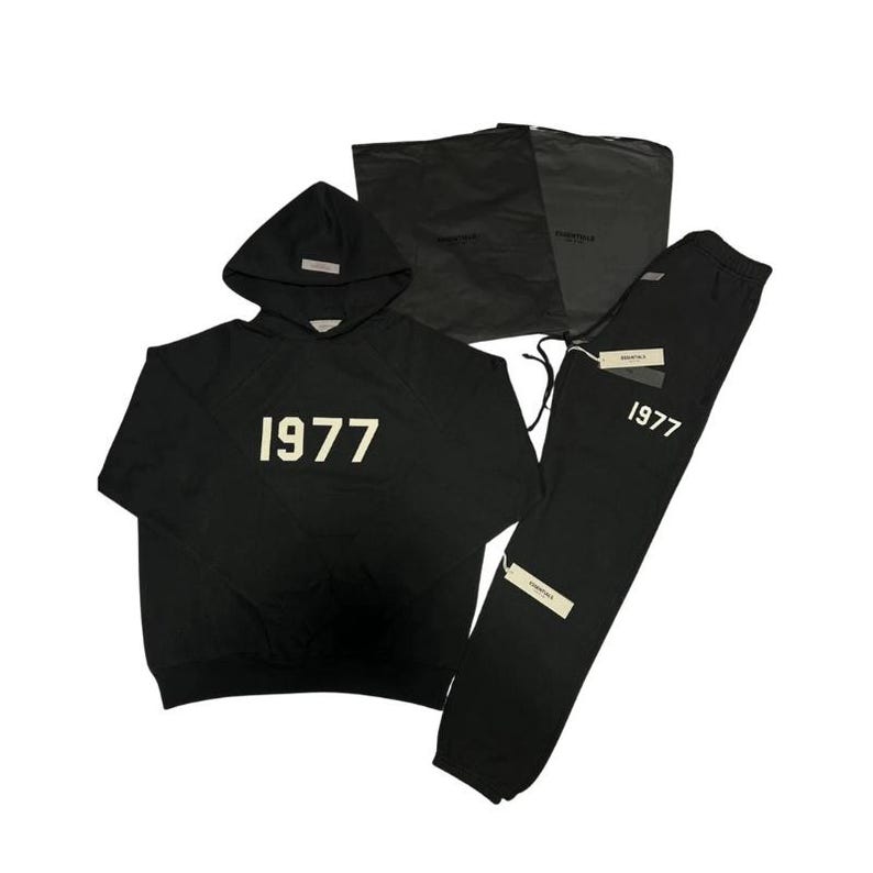 Pu&ograve; includere: Set nero composto da felpa con cappuccio e pantaloni della tuta con il numero "1977" stampato in bianco. La felpa ha un cappuccio e una piccola etichetta. I pantaloni della tuta hanno un cordino e un'etichetta. &Egrave; inclusa anche una borsa nera.