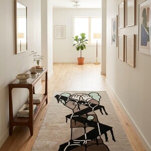 Abstract character hand tufted wool rug displayed in a bright hallway, modern designer area rug with black graphic artwork on a neutral cream background.