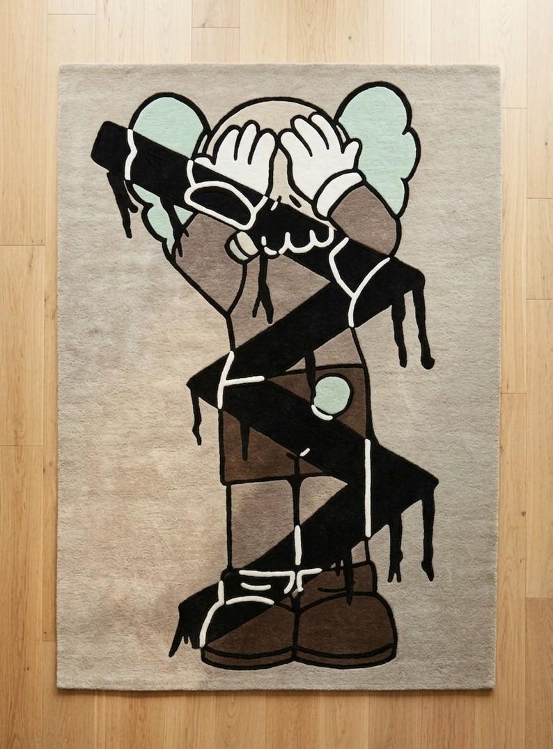 Overhead view of abstract designer rug featuring bold character artwork, contemporary statement carpet in neutral beige, black, and brown tones.