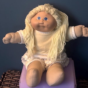 May include: A white ceramic mug with a black handle and the text "But First, Coffee" in a bold, black font. The mug is set against a blurred background, suggesting a cozy setting.