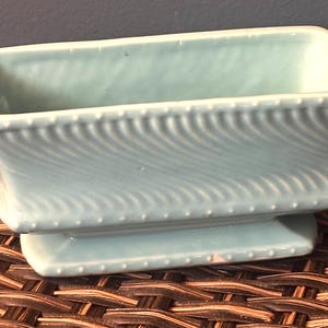 May include: A light blue rectangular ceramic planter with a wavy pattern on the sides and a dotted border. The planter sits on a matching base, perfect for small plants or succulents.