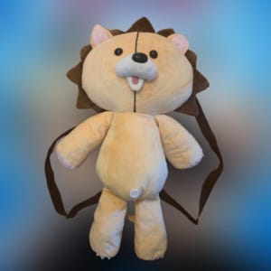 May include: A tan and brown plush lion backpack. The lion has a smiling face with black eyes, a white mouth, and pink inner ears. The backpack has brown straps and a small white button on the back.