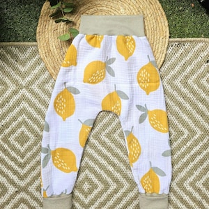 Op de afbeelding: Witte broek met een herhalend patroon van gele citroenen met grijze bladeren. Het kledingstuk heeft een brede, geribbelde, saliegroene elastische tailleband en bijpassende geribbelde enkelboorden. De stof heeft een gekreukte textuur.