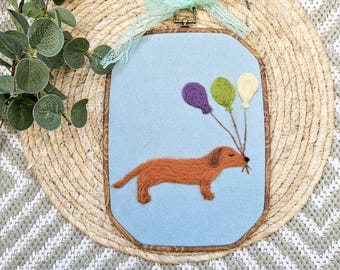 Handmade felt picture of a dachshund with balloons. Decorative felt dog picture made of merino wool on light blue cotton corduroy. Felted wall art for hanging.