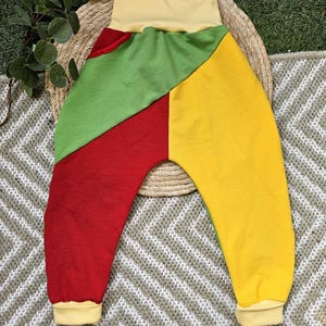 Könnte beinhalten: Bunte Babyhose in Rot, Grün und Gelb, mit gelbem Bund und Bündchen. Die Hose ist aus weichem Stoff gefertigt und auf Komfort ausgelegt. Das Patchwork-Design verleiht dem Kleidungsstück eine verspielte Note.