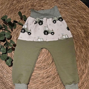 Könnte beinhalten: Olivgrüne Babyhose mit einem hellrosa Oberteil mit grünen Traktoren. Der Bund und die Bündchen sind dunkelgrün mit horizontalen Streifen. Die Hose aus weichem Stoff ist auf Komfort ausgelegt.