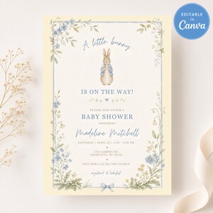Könnte beinhalten: Eine Babyparty-Einladung mit hellgelbem Hintergrund und blauem Blumenrand. Die Einladung zeigt eine Illustration eines Hasen und den Text "A little bunny is on the way!" sowie Details für Madeline Mitchells Babyparty.