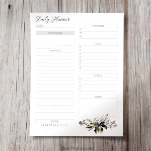 May include: A printable daily planner with sections for inspiration, schedule, priorities, to do, meals, notes, and water intake. The planner has a floral design in black and green watercolor.