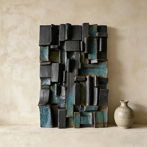 May include: Abstract wall art with a textured, geometric design in shades of black and teal. The artwork is composed of rectangular blocks, creating a three-dimensional effect. A small, beige ceramic vase sits nearby.