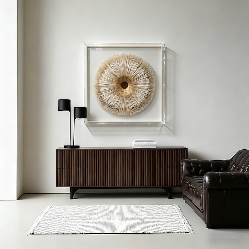 May include: A modern living room setup featuring a dark brown wooden cabinet with vertical grooves, a black lamp, and a framed circular art piece in neutral tones. A white rug and a brown leather sofa complete the scene.