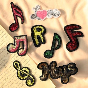 May include: Assortment of sequined patches in various shapes and colors. Includes musical notes in red, pink, and green, a yellow treble clef, the letter "R", the word "Love" with a pink heart, and the word "Hys".