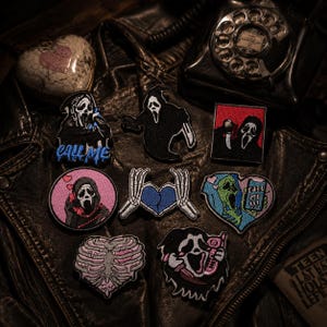 May include: A collection of eight embroidered patches featuring horror-themed designs, including figures in black cloaks with white masks, skeleton hands forming a heart, and a ribcage heart, with text reading CALL ME and CALL ME.