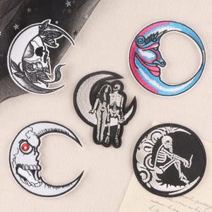 May include: Five embroidered patches featuring celestial and skeletal motifs. One shows a skull with leaves on a crescent moon, another a colorful moon face, a third a skeleton and figure on a moon, a fourth a skull with a red eye, and a fifth a skeleton on a moon.