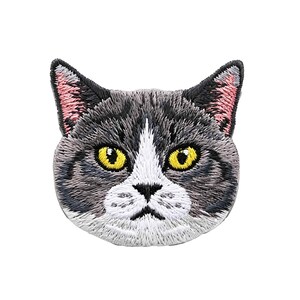 Puede incluir: Un parche bordado con forma de cabeza de gato con pelaje gris y blanco. El gato tiene ojos de color amarillo brillante, nariz negra y el interior de las orejas de color rosa. El bordado crea una apariencia texturizada que resalta los rasgos.
