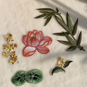 May include: Embroidered patches featuring floral and botanical designs. Includes a red lotus flower, green bamboo leaves, and various flower and leaf clusters in shades of yellow, green, and red. Perfect for adding to clothing or accessories.