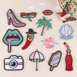 May include: A collection of embroidered patches featuring various designs. Includes a high-heeled shoe, dragonfly, lips, palm tree, bird, seashell, chili pepper, planet, camera, umbrella, popsicle, and a bottle with a straw. The patches are in various colors.