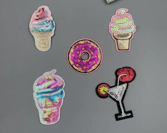 Könnte beinhalten: Eine Sammlung von Pailletten-Patches mit Eiswaffeln, einem Donut und einem Cocktail. Die Patches sind in verschiedenen Farben, darunter Rosa, Gold und Blau. Die Patches befinden sich auf einem grauen Hintergrund.