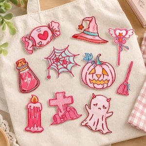 Puede incluir: Un conjunto de diez parches bordados termoadhesivos con diseños de Halloween en rosa y azul claro, que incluyen un caramelo, sombrero de bruja, varita mágica, telaraña, poción, calabaza, escoba, vela, cruz y un fantasma.