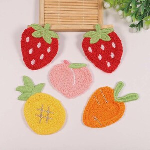 May include: Five embroidered fruit patches: two red strawberries with green tops and white seeds, a pink peach, a yellow pineapple with a green top, and an orange carrot with a green top. Perfect for customising clothes or accessories.