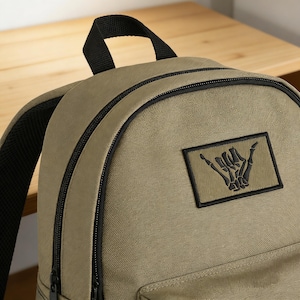 Pode incluir: Uma caneca de cerâmica branca com uma alça preta e o texto "But First, Coffee" em preto, em negrito. A caneca está sobre uma superfície branca. A caneca tem aproximadamente 10 cm de altura.