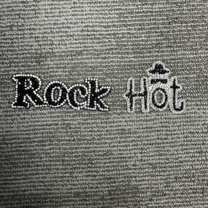 Op de afbeelding: Twee opstrijkbare patches met de woorden Rock en Hot. De letters zijn gevuld met zwart materiaal en omlijnd met heldere, reflecterende strass-steentjes. Het woord Hot bevat een klein, met strass ingelegd hoed-icoontje boven de o.