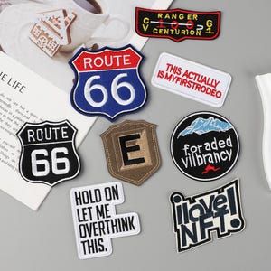 Può includere: Una collezione di toppe ricamate con vari disegni e testo. Include un cartello della Route 66, una toppa con la scritta "This Actually Is My First Rodeo" e una toppa con la scritta "I love NFT!"