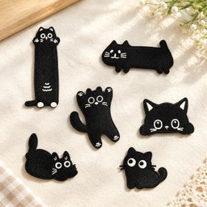 Puede incluir: Un conjunto de seis parches bordados negros con forma de gato en varias posturas, incluyendo un gato vertical largo, uno horizontal, uno con las patas levantadas, uno asomándose, uno tumbado y un pequeño gato sentado, con detalles en blanco.