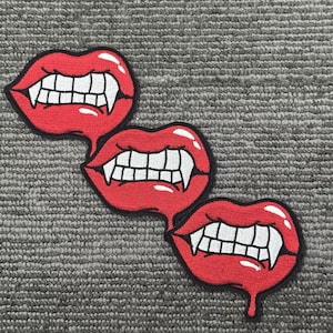 Op de afbeelding: Drie rode geborduurde patches in de vorm van open monden met scherpe tanden. De patches hebben witte tanden en een glanzende afwerking. De patches zijn zwart omlijnd en lijken te druipen.