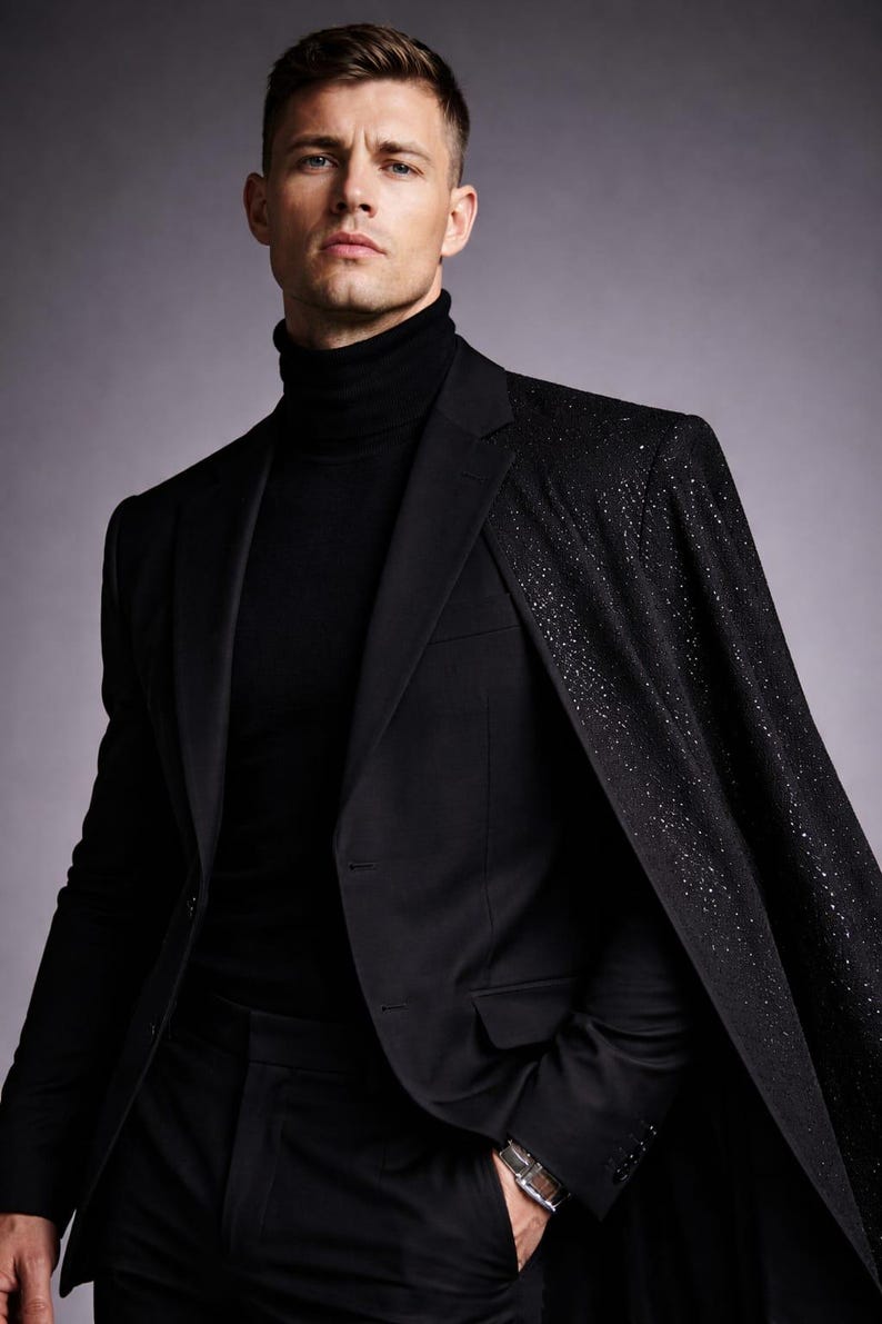 Puede incluir: Un traje negro con un cuello alto negro a juego. La chaqueta del traje presenta un dise&ntilde;o tipo capa con un patr&oacute;n brillante en los hombros. Se ve un reloj plateado.