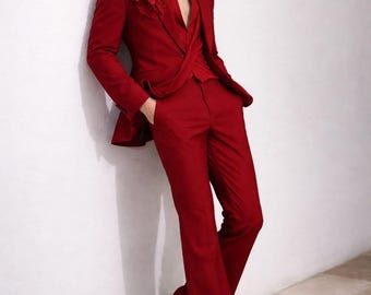 May include: A striking red suit with a floral accent on the lapel. The suit features a tailored jacket and flared trousers, paired with matching red shoes. The outfit is a bold fashion statement.