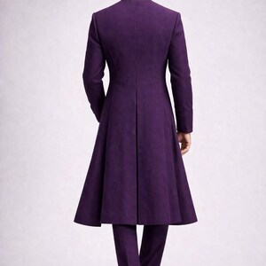 May include: A full-length, purple suit with a long coat and matching trousers. The coat has a high collar and a flared skirt. The trousers are straight-legged. The suit is made of a smooth fabric and is worn with black shoes.