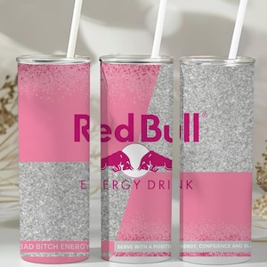 May include: Three tall, pink and silver tumblers with white straws. The tumblers feature the Red Bull logo and text, with the words "BAD BITCH ENERGY" and "SERVE WITH A POSITIVITY" printed on them. The design includes a pink and silver glitter pattern.