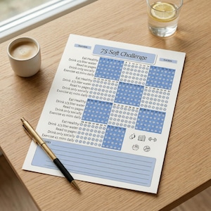 May include: A printed 75 Soft Challenge tracker on a wooden surface. The tracker includes a blue and white grid with checkboxes, and instructions to eat healthy, drink water, read, and exercise. A pen, coffee, and a glass of water are also present.