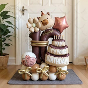 May include: A celebratory balloon display in brown and beige tones, perfect for a birthday. The arrangement includes balloons shaped like a bear, a flower, and a star. A balloon cake reads "Yay It's Your Birthday!" and the name "Laylah" is also present.