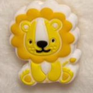 May include: A yellow and white lion-shaped embellishment with a friendly expression. The lion has a yellow mane, paws, and a white face and body. The embellishment is likely made of a soft material.