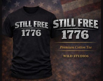 May include: Black t-shirt with the text "STILL FREE 1776" in distressed white lettering. The words "Premium Cotton Tee" and "WILD STUDIOS" are also visible. The background features an American flag.