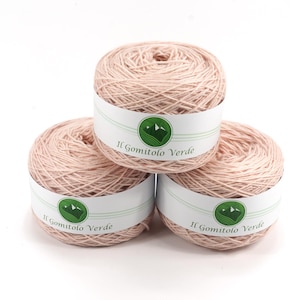 May include: Three balls of light pink yarn are stacked on a white background. Each ball has a white label with the text "Il Gomitolo Verde" and a green mountain logo. The yarn appears soft and is tightly wound.