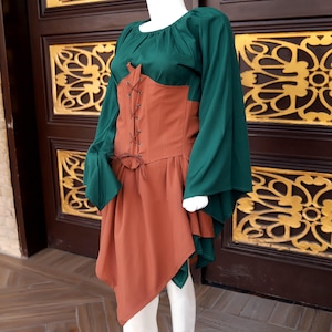 Op de afbeelding: Een groen en roestkleurig middeleeuws ge&iuml;nspireerde jurk op een mannequin. De jurk heeft lange, vloeiende groene mouwen, een roestkleurig lijfje met een veter aan de voorkant en een bijpassende asymmetrische rok. De jurk is ontworpen om een historische of fantasie-esthetiek op te roepen.