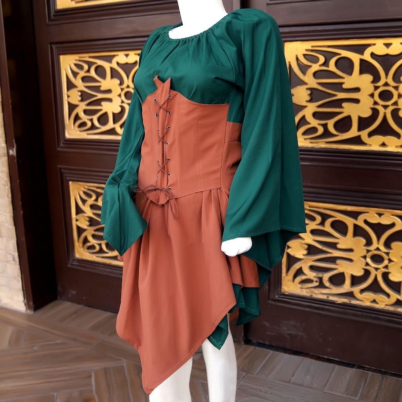 Op de afbeelding: Een groen en roestkleurig middeleeuws ge&iuml;nspireerde jurk op een mannequin. De jurk heeft lange, vloeiende groene mouwen, een roestkleurig lijfje met een veter aan de voorkant en een bijpassende asymmetrische rok. De jurk is ontworpen om een historische of fantasie-esthetiek op te roepen.