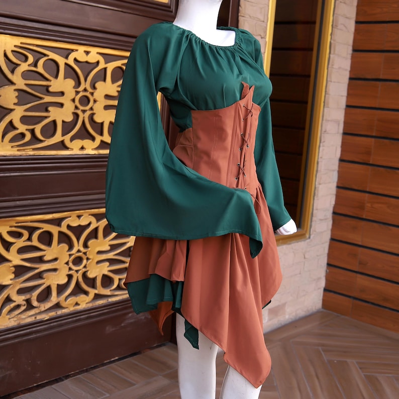 Op de afbeelding: Een groene en bruine jurk in middeleeuwse stijl. De top is groen met lange, uitlopende mouwen. Een bruin lijfje in korsetstijl wordt aan de voorkant geregen. De rok is gelaagd, met een bruine asymmetrische zoom en een groene onderrok.