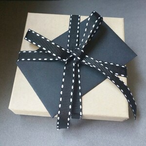 Puede incluir: Una caja de regalo marr&oacute;n con una cinta negra y blanca atada en un lazo. La cinta tiene lunares blancos.