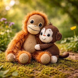 May include: Two crocheted monkey plush toys. One is larger, with orange fur and a tan face. The smaller monkey is brown and white, hugging the larger one. Both have large black eyes and are sitting on a bed of green moss.