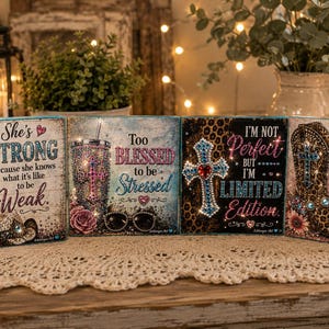 May include: Four square wooden signs featuring decorative rhinestone accents and inspirational text. The designs include a glittery tumbler, a cross, and a cowboy boot, with phrases like She's Strong, Too Blessed to be Stressed, I'm Not Perfect, and Too Glam to give a Damn.