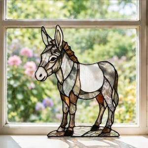 May include: A stained glass donkey figure constructed from various shades of gray, white, and brown glass pieces joined by dark metal lines. The donkey stands on a flat base, featuring a white patch on its side and pointed ears.