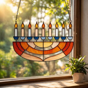 Puede incluir: Menorá de vidriera con nueve candelabros, cada uno con una vela encendida. La menorá presenta un diseño semicircular con vidrio naranja, amarillo y rojo. Cuelga de una cadena frente a una ventana.